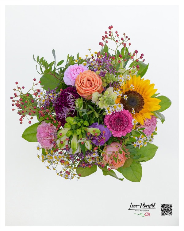Dieser farbenfrohe Blumenstrauß kombiniert die leuchtende Wärme einer Sonnenblume mit der zarten Eleganz von Rosen, den verspielten Blüten der Kamille, der auffälligen Schönheit von Gerbera, den kräftigen Nelken, den charmanten Löwenmäulchen und den dekorativen Hagebutten, um eine harmonische und lebendige Komposition zu schaffen.