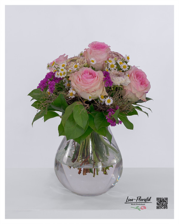 Strauß mit hochwertigen Ecuador-Rosen in rosa, kombiniert mit kleinen weißen Kamilleblüten, violettem Strandflieder und zart cremefarbenen Ranunkeln mit feiner Zeichnung. Umrahmt von frischem Grün und lockerem Beiwerk, natürlich und liebevoll gebunden