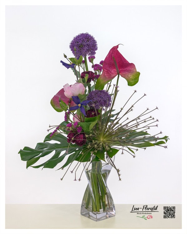 Moderner Blumenstrauß mit auffälligem Allium, darunter auch eine sternförmig explodierende Allium-Schuberti-Blüte. Ergänzt wird das Arrangement durch leuchtend pinke Anthurien, zarte rosa Pfingstrosen, tiefviolette Clematis und kleine, filigrane Statice-Blüten – kombiniert mit großflächigem Grün für einen expressiven, skulpturalen Look.