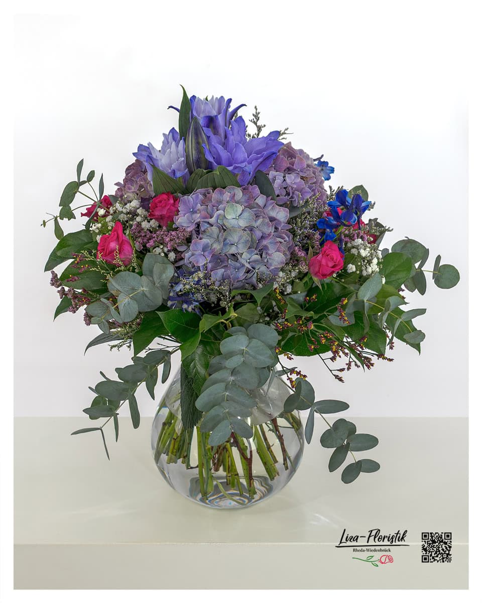 Üppiger Blumenstrauß mit lila Hortensien, pinken Rosen, violetten Lilien, blauem Rittersporn, Schleierkraut, Statice und frischem Eukalyptus – ideal als Geschenk oder Dekoration.